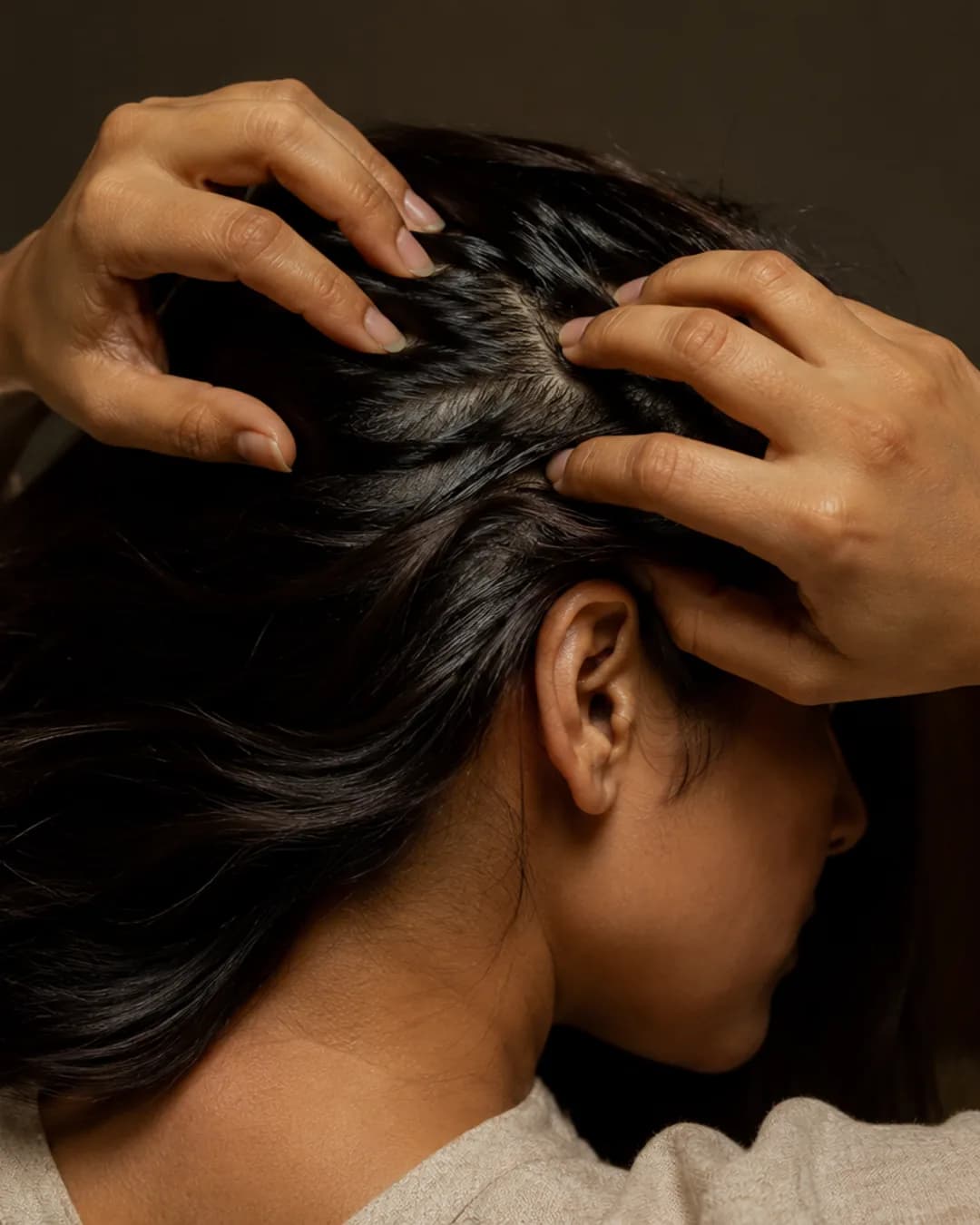 Hands working hair oil into the scalp with the fingertips